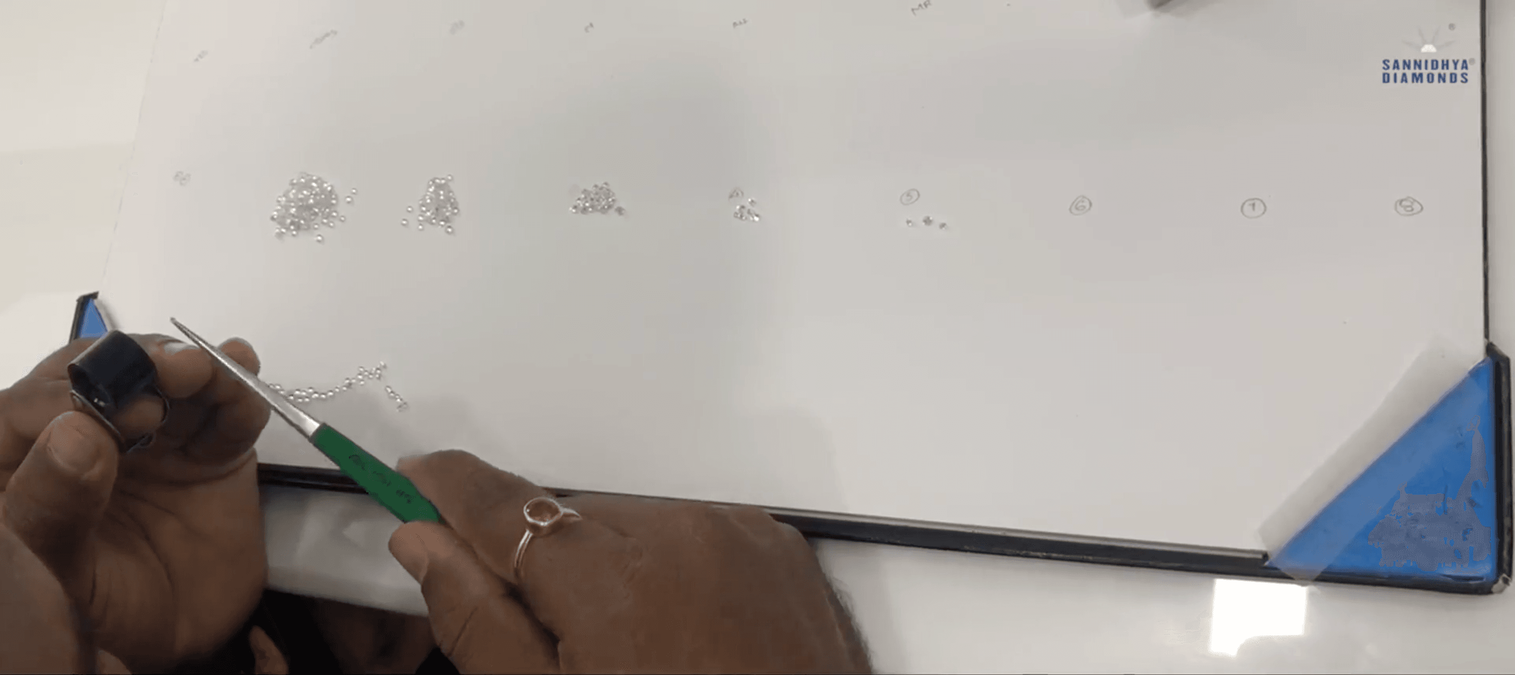 Hands sorting small diamonds into precisely graded piles during quality assortment